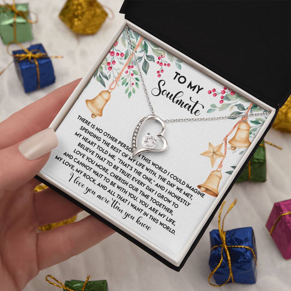 A hand holds an open box showcasing the elegant Soulmate-Be With You - Forever Love Necklace, beautifully adorned with CZ crystals and a white gold finish. Inside, a card embellished with festive designs contains a heartfelt message addressed to "My Soulmate.