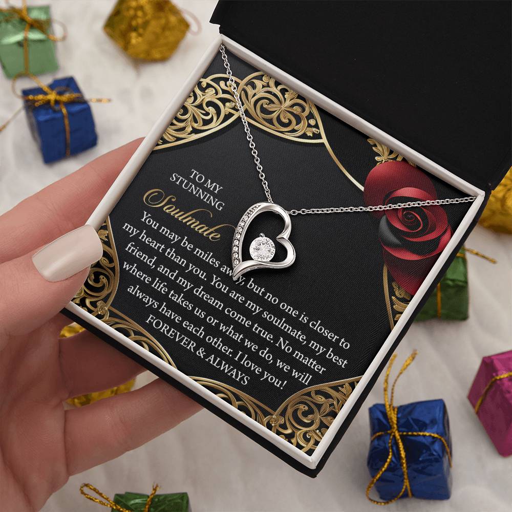 A hand opens a jewelry box to reveal the Soulmate-Have Each Other - Forever Love Necklace, featuring a heart-shaped pendant with a sparkling cubic zirconia stone. The box is adorned with an elegant romantic message in gold and red detailing.