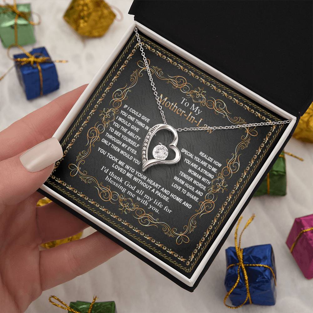 A hand holds an open jewelry box containing the "To Mother-In-Law, Through My Eyes - Forever Love Necklace" with a message to "My Mother-in-Law," surrounded by small colorful gift boxes. The perfect gift for your mom or mother-in-law!