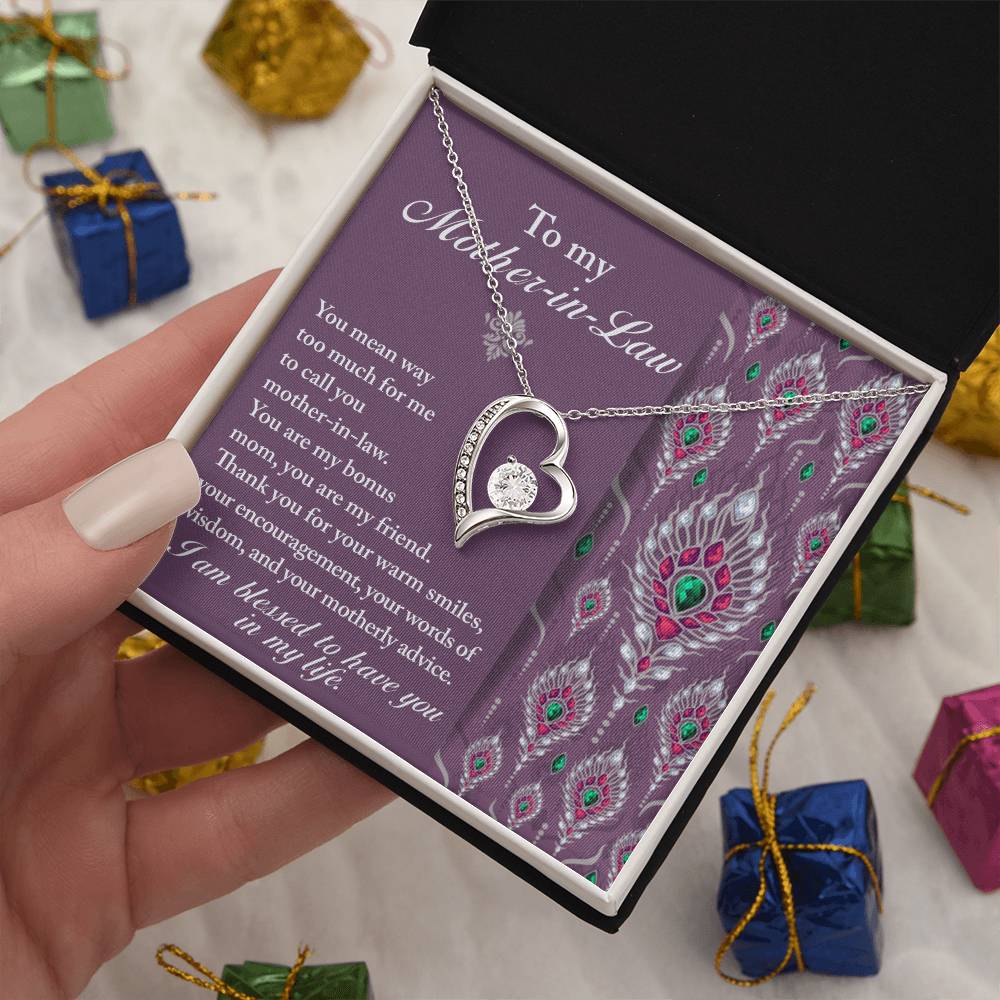 A person holds an open gift box containing a heart-shaped, "To Mother-In-Law, Words Of Wisdom - Forever Love Necklace" along with a sentimental message to their mother-in-law. The background includes small, wrapped gifts.