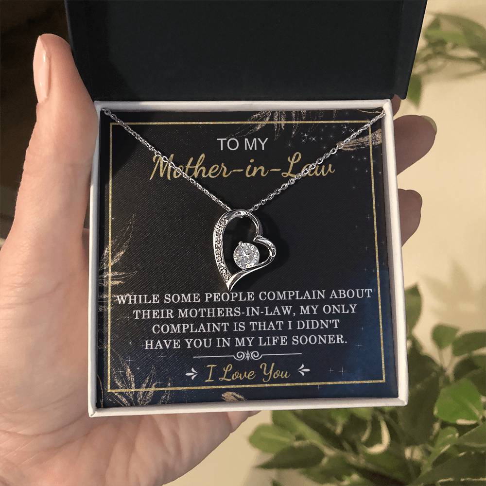 A hand holds an open jewelry box containing the "To Mother-In-Law, In My Life - Forever Love Necklace," a heart-shaped necklace adorned with a cubic zirconia stone. The message inside reads, "To my Mother-in-Law, my only complaint is that I didn’t have you in my life sooner. I love you.
