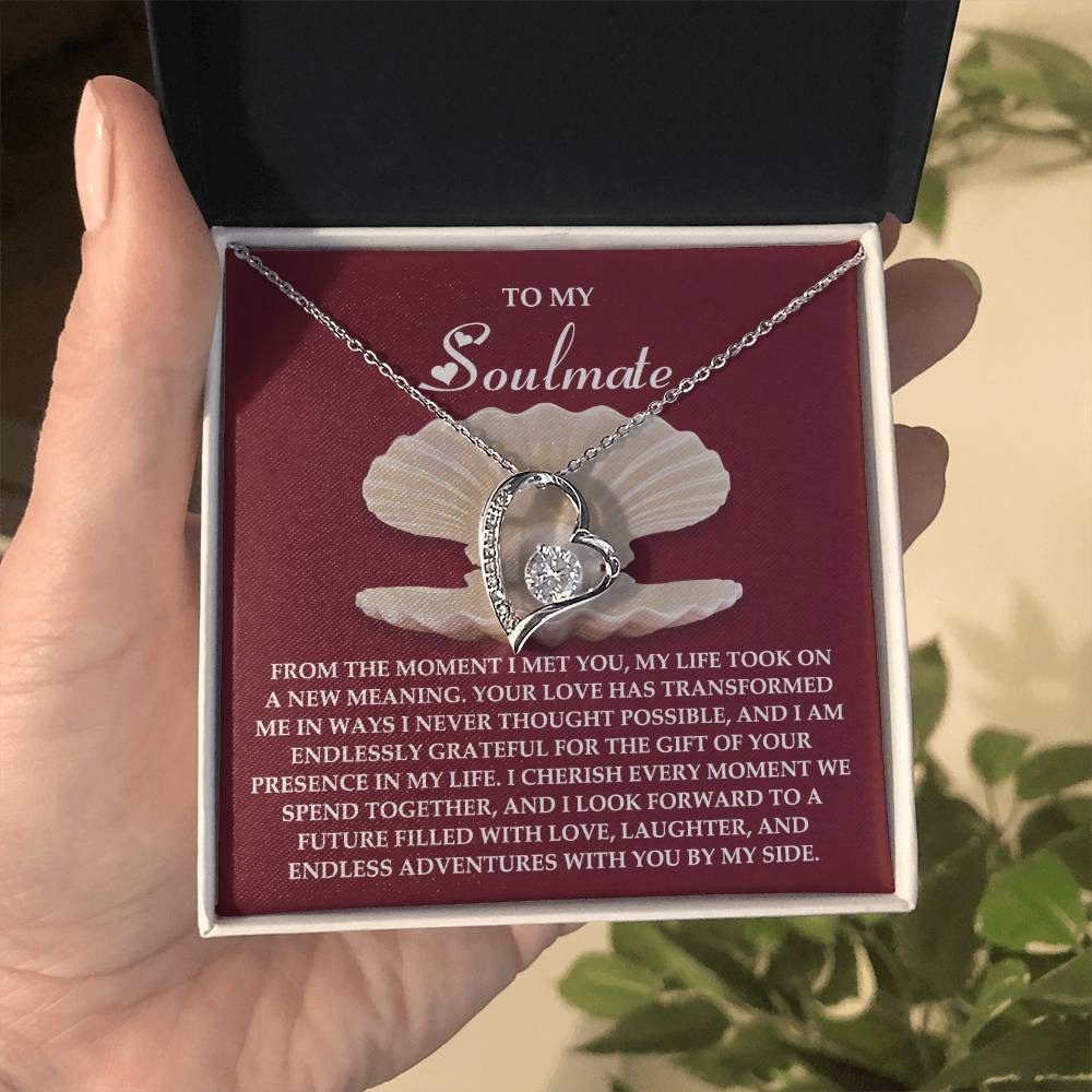 A hand cradles an open jewelry box, revealing the stunning Soulmate-Every Moment - Forever Love Necklace. Its shimmering white gold finish catches the light, accompanied by a heartfelt message to a soulmate.