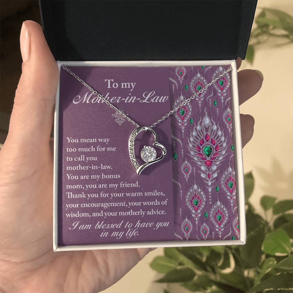 A hand holding a beautifully wrapped gift box with the "To Mother-In-Law, Words Of Wisdom - Forever Love Necklace" inside. The Forever Love Necklace features a heart-shaped pendant, and the box includes an appreciative message to a beloved mother-in-law.
