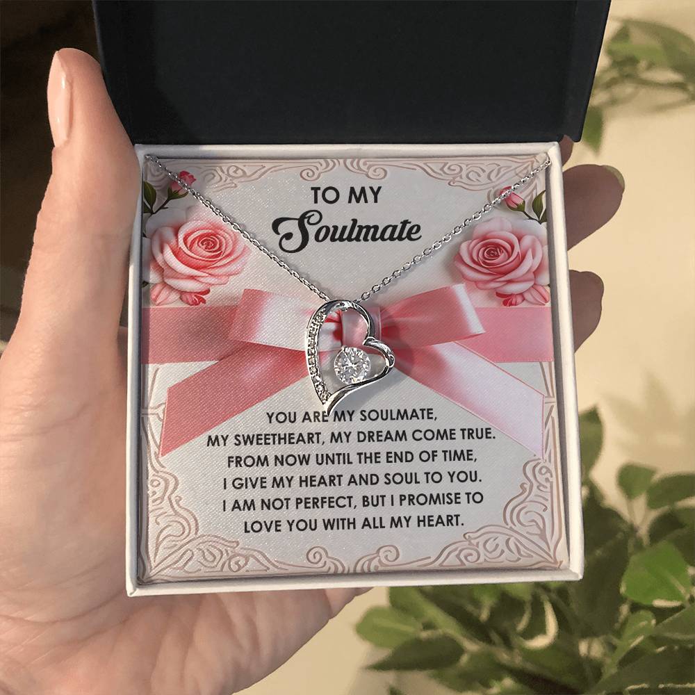 A hand presents an open box with the elegant Soulmate-Heart and Soul - Forever Love Necklace, featuring a heart-shaped pendant adorned with CZ crystal and gold finish, resting next to a card with a romantic message, all surrounded by decorative roses.