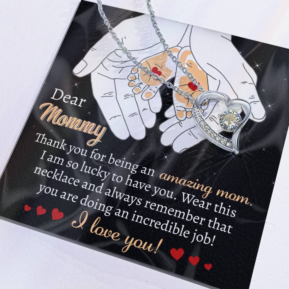 The "To Mom To Be, An Incredible Job - Forever Love Necklace" features a heart-shaped pendant on a silver chain, resting on a card that reads: "Dear Mommy, Thank you for being an amazing mom. I am so lucky to have you. I love you!" adorned with illustrated hands and hearts. This personalized gift is a timeless expression of love and gratitude.