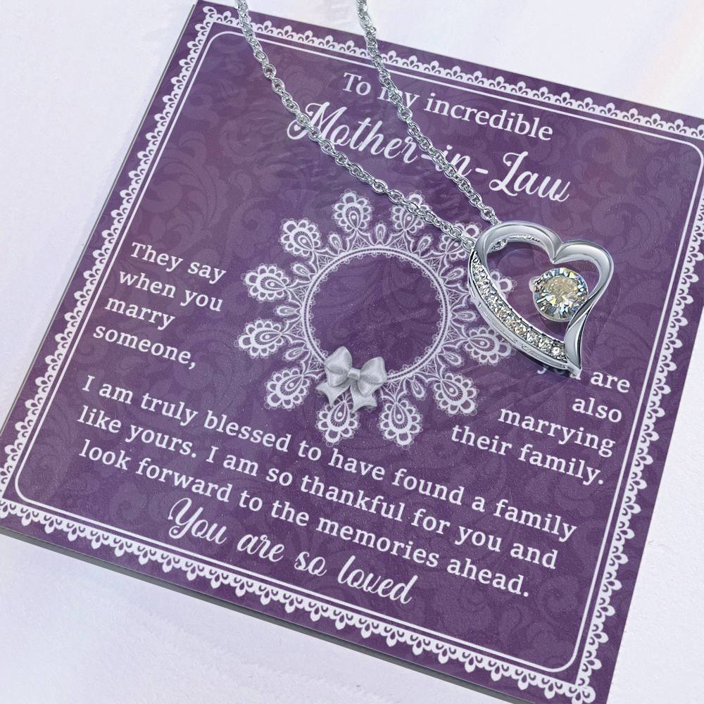 The "To Mother-In-Law, Family Like Yours - Forever Love Necklace" is a silver heart-shaped necklace featuring a diamond pendant and a 14k white gold finish. It is elegantly displayed on a purple card that reads "To my incredible Mother-in-Law" along with a heartfelt message about love and family, making it a unique gift she'll cherish forever.