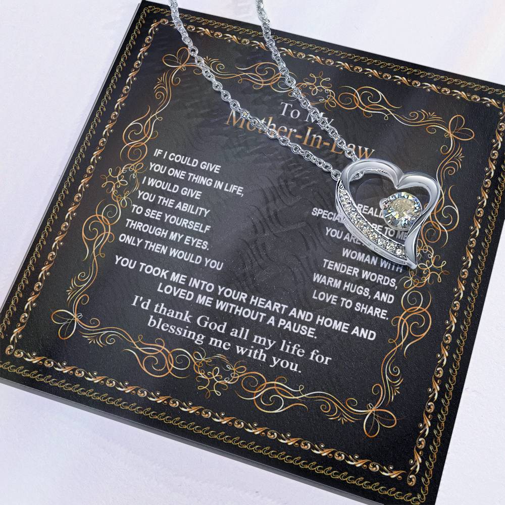 The "To Mother-In-Law, Through My Eyes - Forever Love Necklace," a silver heart-shaped pendant, rests on an ornate black card adorned with a heartfelt message to your mother-in-law in elegant gold and white text—the perfect gift for your mom.