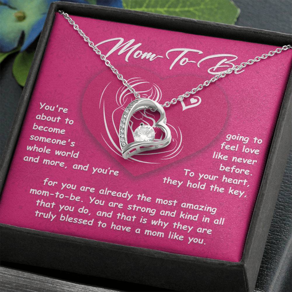 The "To Mom To Be, Someone's Whole World - Forever Love Necklace," a silver heart pendant, is elegantly presented in a gift box with a pink background. Accompanying it is a heartfelt note that congratulates the mom-to-be and highlights love, support, and appreciation for her.