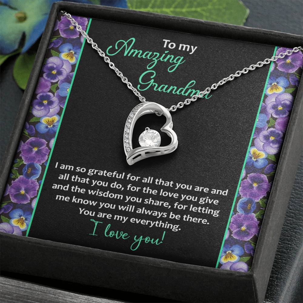 The "To Grandma, My Everything - Forever Love Necklace" features a heart-shaped pendant showcased beautifully on a card adorned with a floral border. The card includes a heartfelt appreciation message for a grandmother, expressing love and gratitude. The stunning pendant is embellished with a sparkling cubic zirconia stone set in 14k white gold finish.