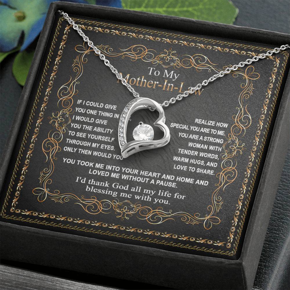 The "To Mother-In-Law, Through My Eyes - Forever Love Necklace" is a silver heart-shaped pendant with a central gemstone on a delicate chain, beautifully displayed in an open gift box. The interior lid features an ornate message for your mother-in-law, making it the perfect gift for her.