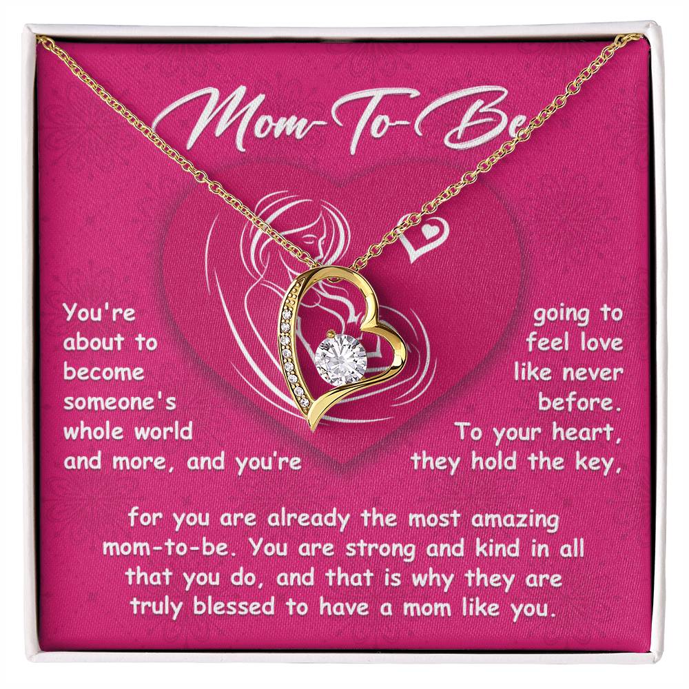 A heart-shaped gold necklace with a diamond pendant is beautifully displayed in a pink box labeled "To Mom To Be, Someone's Whole World," featuring a heartfelt message about becoming a mother. This Forever Love Necklace makes the perfect personalized gift for an expecting mom.