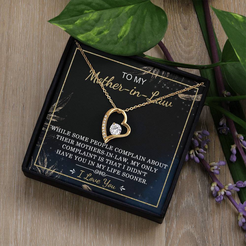 A "To Mother-In-Law, In My Life - Forever Love Necklace" featuring a stunning cubic zirconia stone at its center, beautifully presented in a black box with a heartfelt inscription dedicated to the mother-in-law, surrounded by lush green leaves and delicate purple flowers.