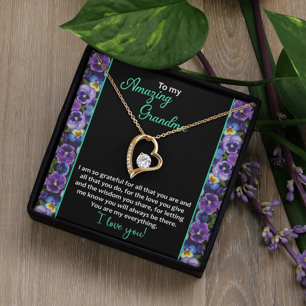 The "To Grandma, My Everything - Forever Love Necklace" features a heart-shaped design with a sparkling cubic zirconia stone in a 14k white gold finish. It comes nestled in a gift box adorned with purple flowers. The heartfelt message reads: "To my Amazing Grandma. I am so grateful for all that you are and all that you do... I love you!