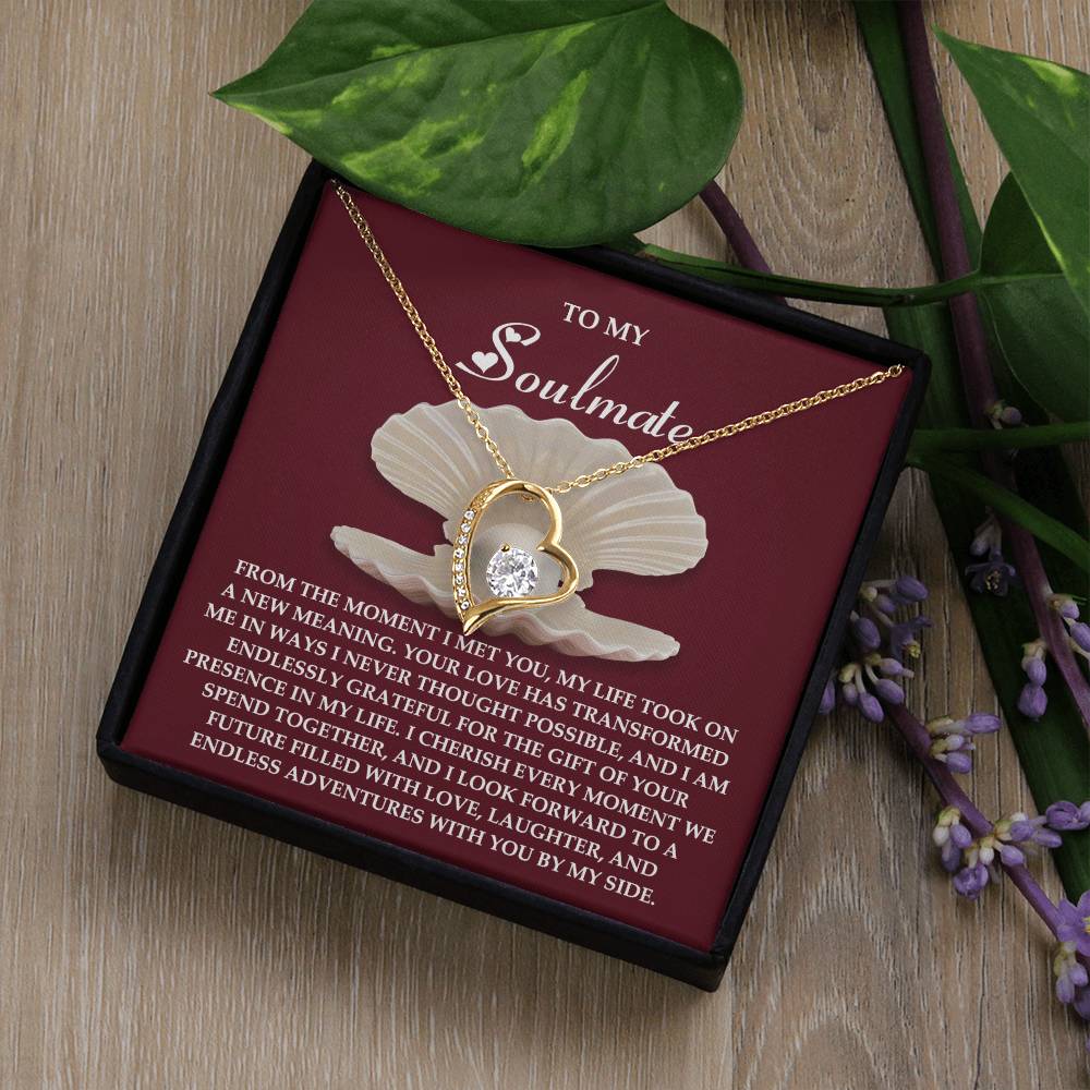 The Soulmate-Every Moment - Forever Love Necklace has a gold heart with a cubic zirconia stone, presented in a box. The card says "To My Soulmate" with green leaves and purple flowers on rustic wood.