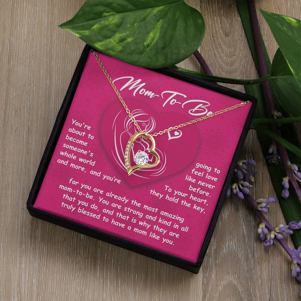 A personalized "To Mom To Be, Someone's Whole World - Forever Love Necklace" featuring a heart pendant displayed in a gift box, surrounded by green leaves and purple flowers. Text on the box offers a heartfelt message to expectant mothers, celebrating this moment of forever love.