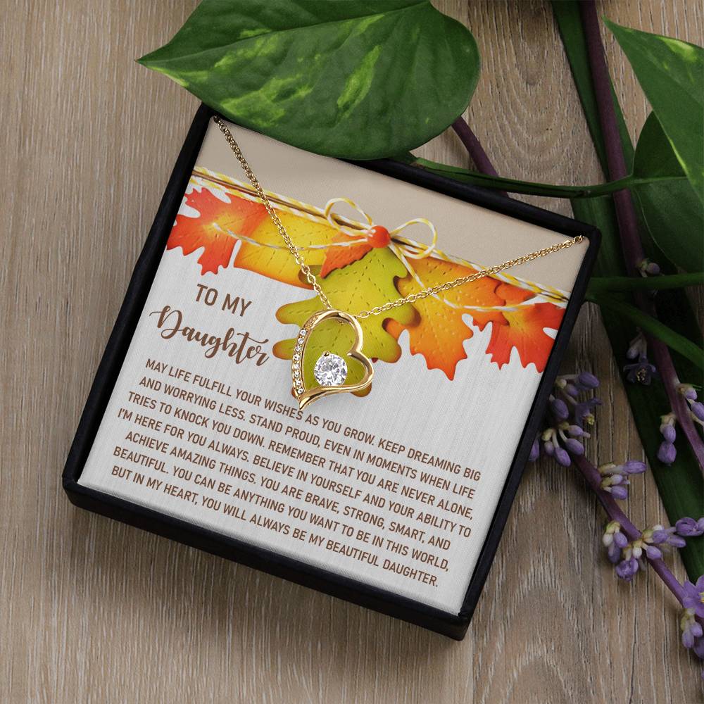 The Daughter-For You Always - Forever Love Necklace is a heart-shaped treasure embellished with CZ crystals and a gold finish, nestled in a gift box with a heartfelt message for your daughter, surrounded by lush greenery and purple flowers.