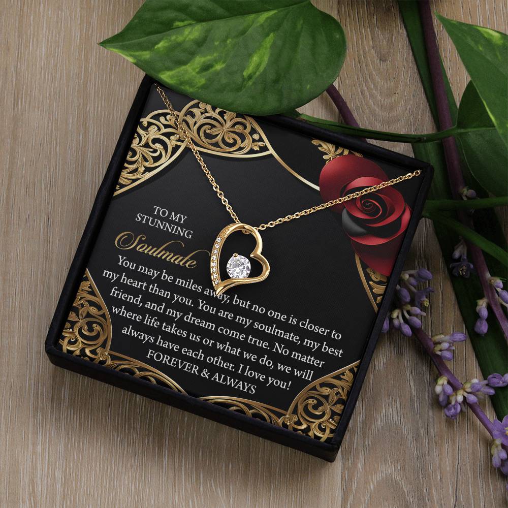 The Soulmate-Have Each Other - Forever Love Necklace, heart-shaped with a gold finish and a sparkling cubic zirconia, elegantly sits on a decorative gift box. A romantic message accompanies it, adorned with purple flowers and green leaves for a captivating touch.