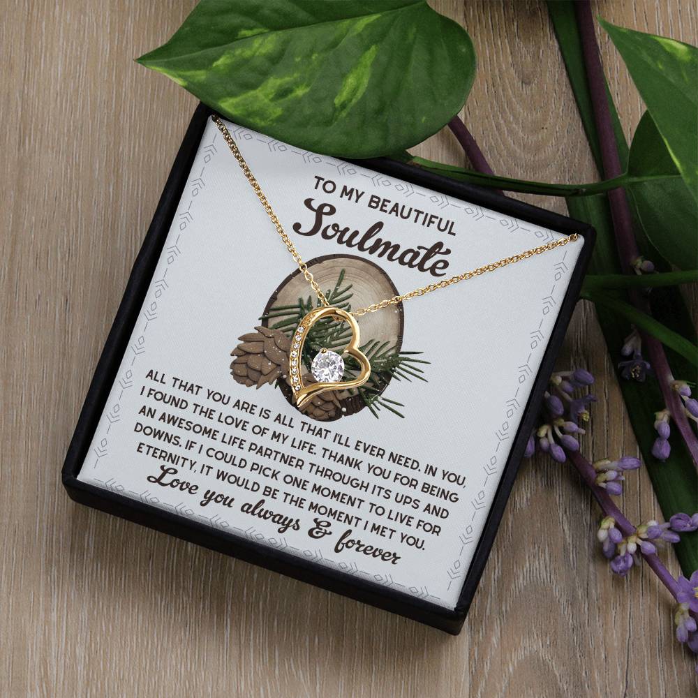 The Soulmate-One Moment - Forever Love Necklace, featuring a radiant cubic zirconia stone in a heart shape, is beautifully presented in a box inscribed with "To My Beautiful Soulmate," and adorned with purple flowers and green leaves.