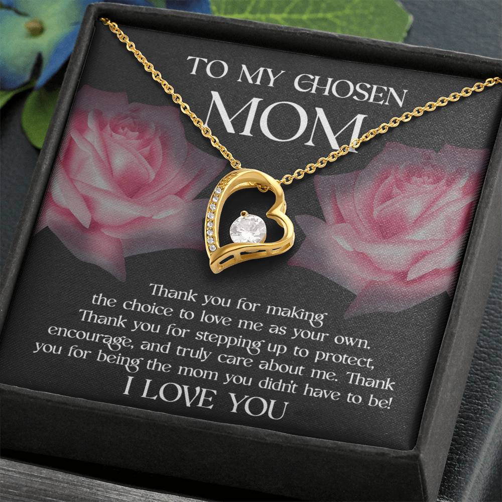 The "To Bonus Mom, My Chosen Mom - Forever Love Necklace" features a gold heart-shaped pendant with a single clear gem at its center. It is elegantly presented in a black box that includes an appreciative message for a "chosen mom," and the card background adorned with pink roses makes it an ideal Mother's Day gift. This necklace is available in both white gold and yellow gold finishes.