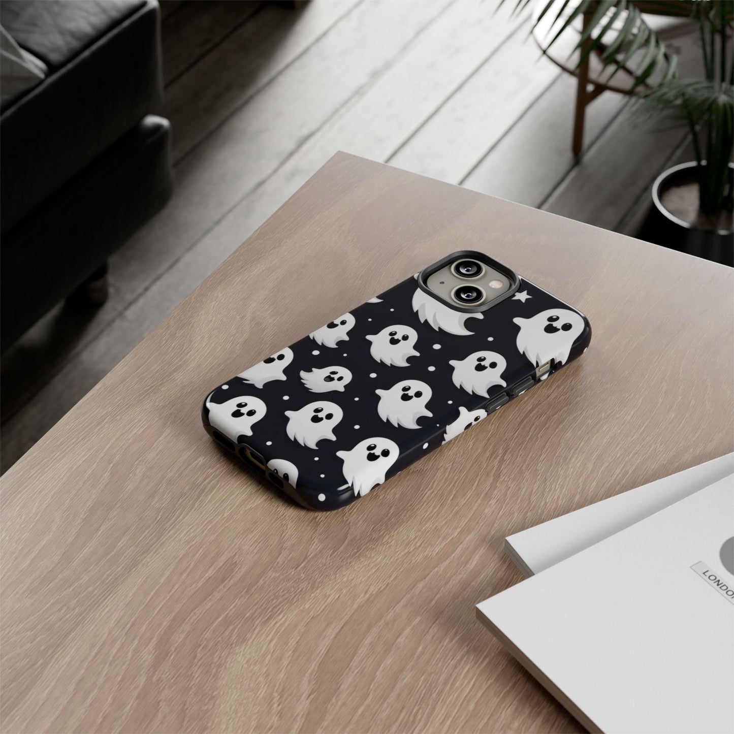 A smartphone adorned with a Creepy Cute Ghosts Case, an ideal Halloween gift for enthusiasts, rests on a wooden table beside a booklet.