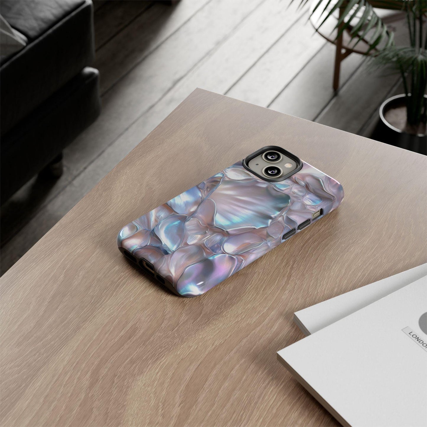 An iPhone equipped with a June Birthstone Mother of Pearl Phone Case lies on a wooden table beside a closed notebook.