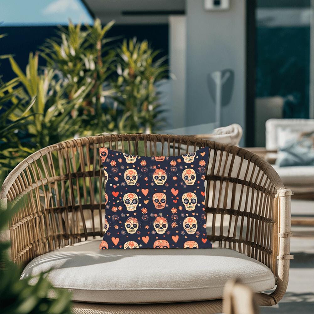 A wicker chair with the vibrant Day of the Dead Mexican Skull Pillow, perfect for Halloween and Dia De Los Muertos decor, sits on a patio framed by lush plants in the background.