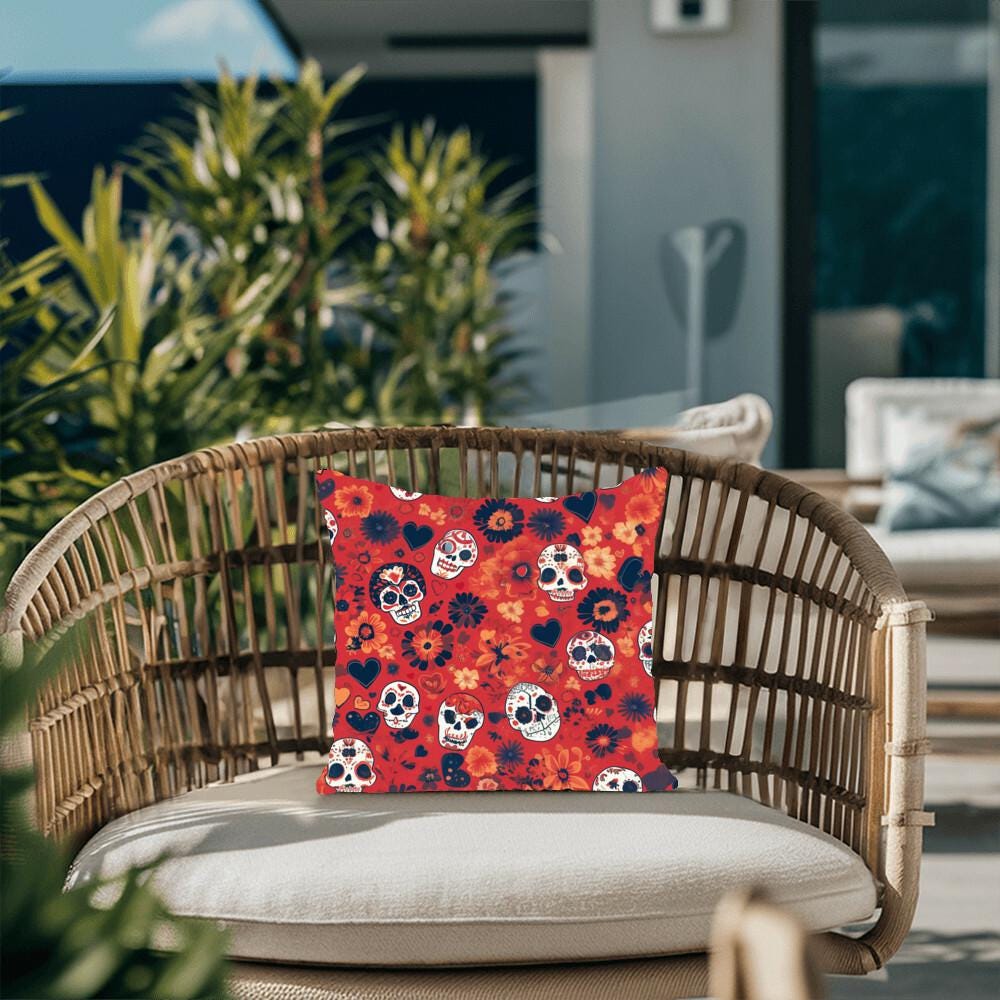 A woven armchair with a vibrant Day of the Dead Mexican Skull Pillow, featuring Halloween and Dia De Los Muertos decor, sits on a sunny patio surrounded by green plants, adding a touch of skull art to the serene setting.