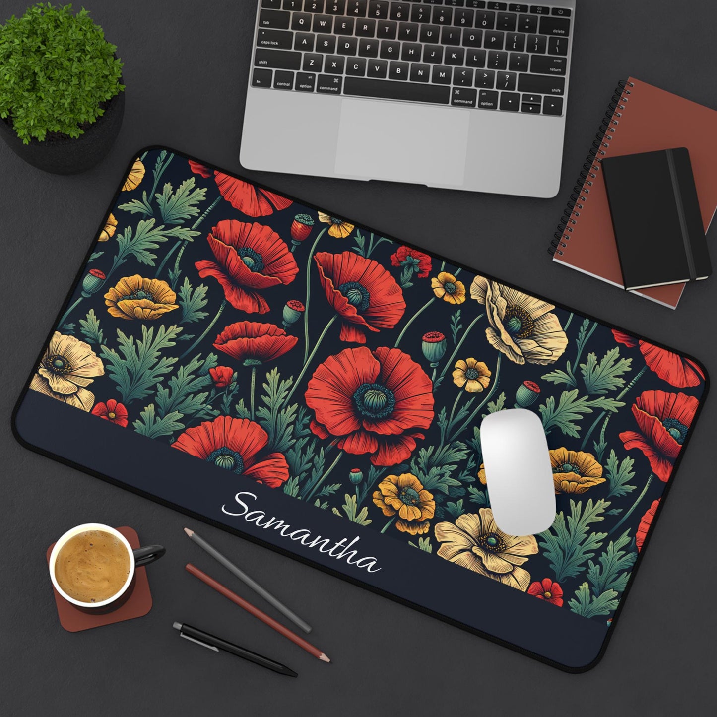 A Personalized Dark Floral Desk Mat, featuring "Samantha" and a botanical design perfect for poppy lovers, adorns the dark surface beside a laptop, notebook, cup of coffee, and two pencils. Its elegant vintage style adds a touch of nature to your workspace.