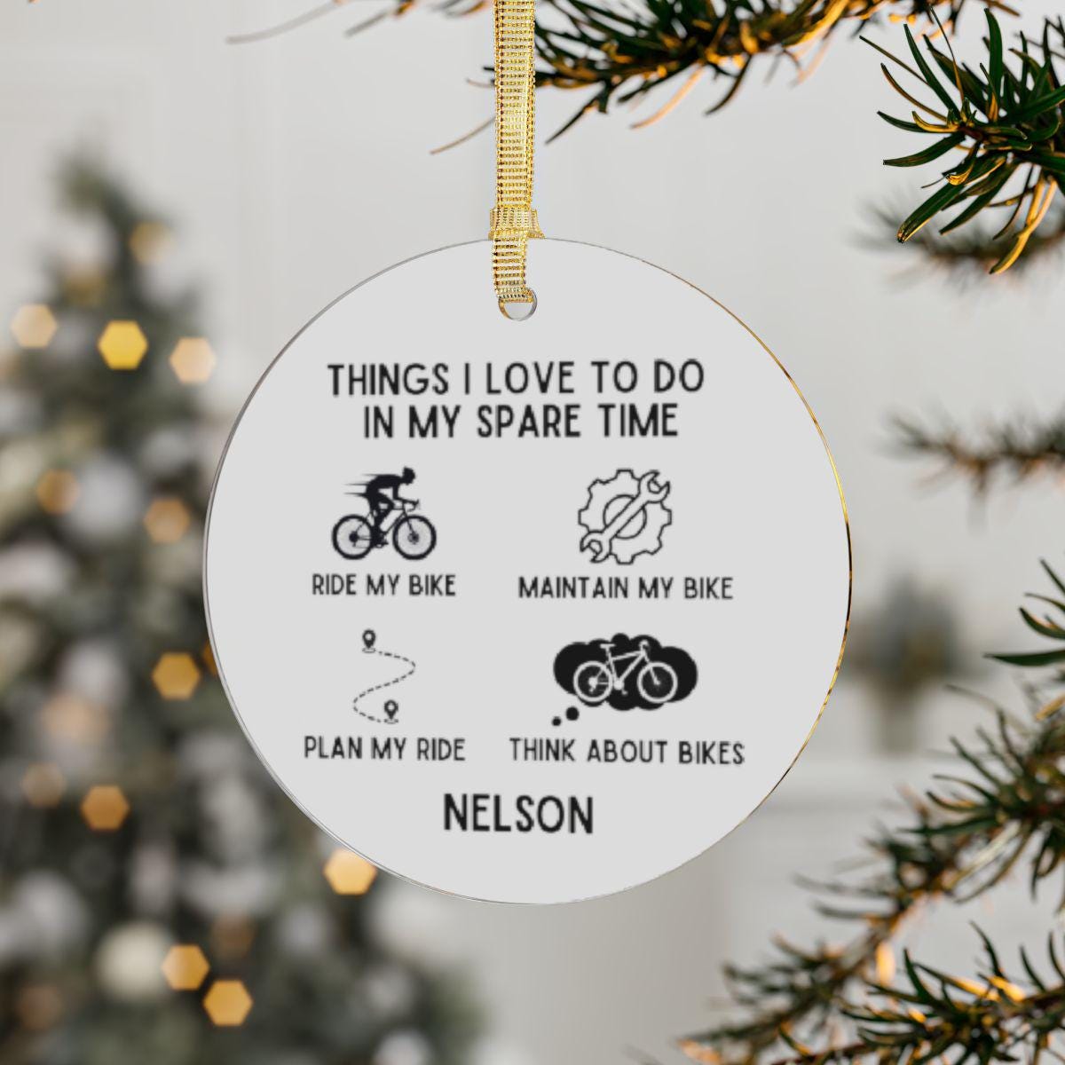 A Personalized Cyclist Ornament, thoughtfully crafted with transparent acrylic, dangles from the Christmas tree. It proudly states: "Things I love to do in my spare time: ride my bike, maintain my bike, plan my ride, think about bikes." This custom name decoration is an ideal festive gift for any cycling lover or bike enthusiast.