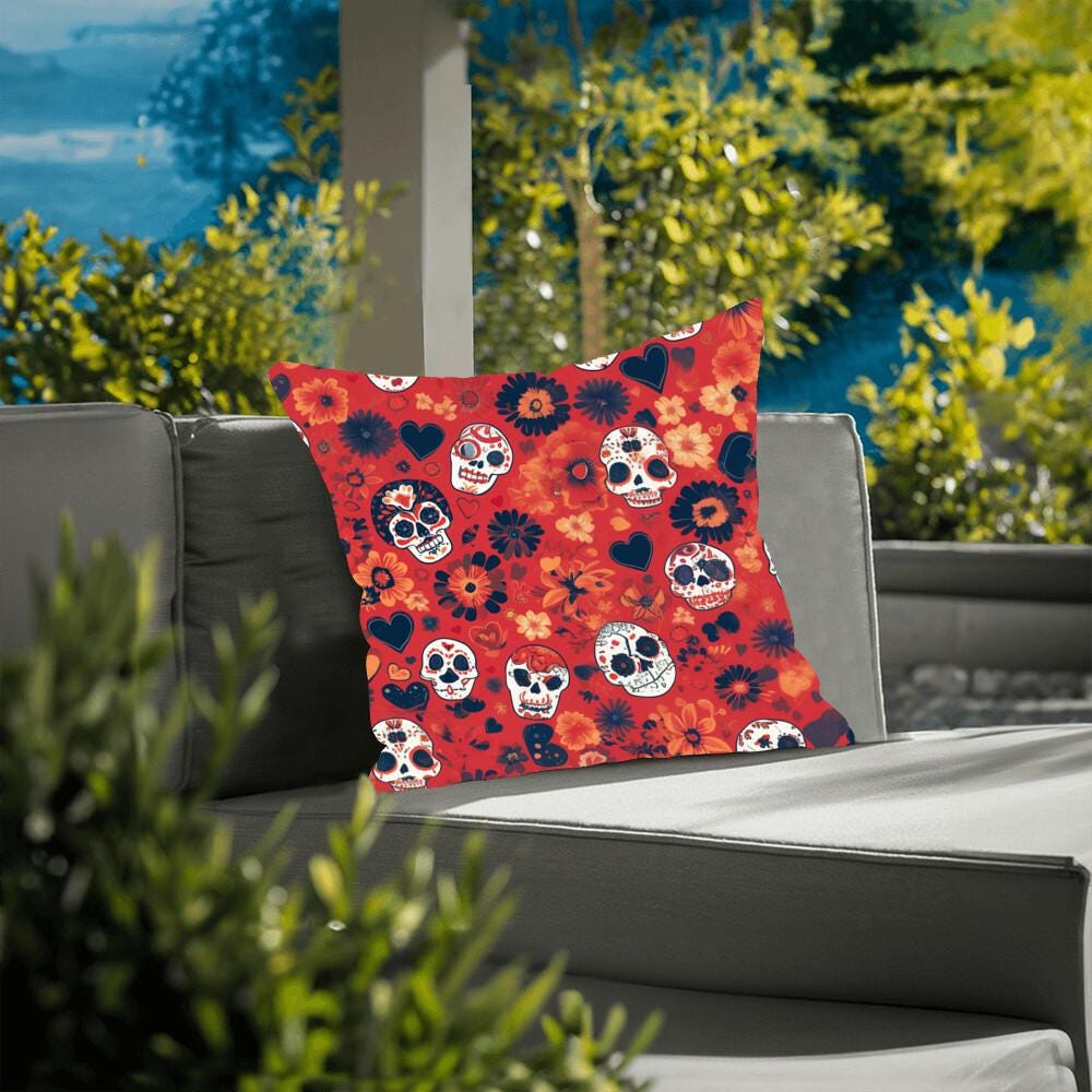 The Day of the Dead Mexican Skull Pillow, featuring skull and floral patterns, enhances the gothic home decor of the gray outdoor sofa, set against a lush backdrop of greenery.