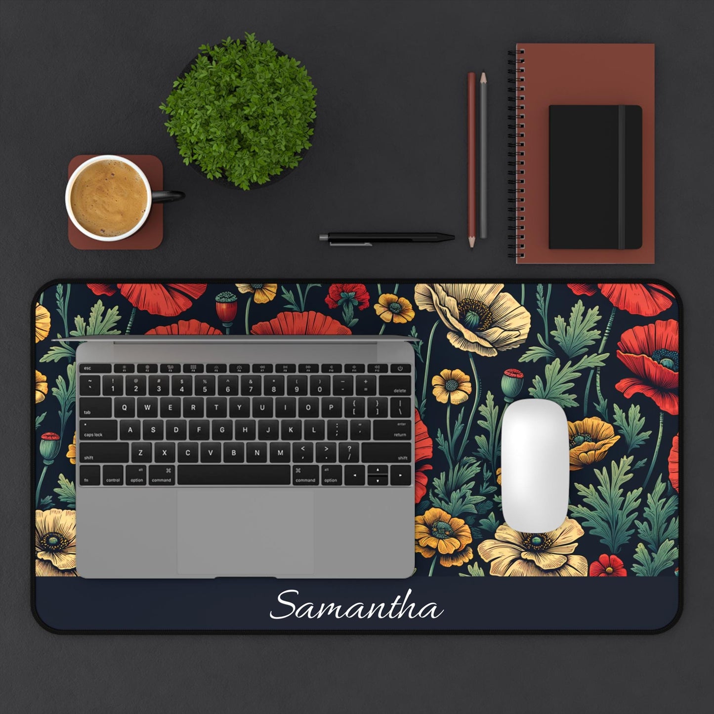 A laptop and mouse rest on a Personalized Dark Floral Desk Mat with "Samantha" inscribed, accompanied by a coffee cup, plant, notebook, and pens that enhance the dark surface.
