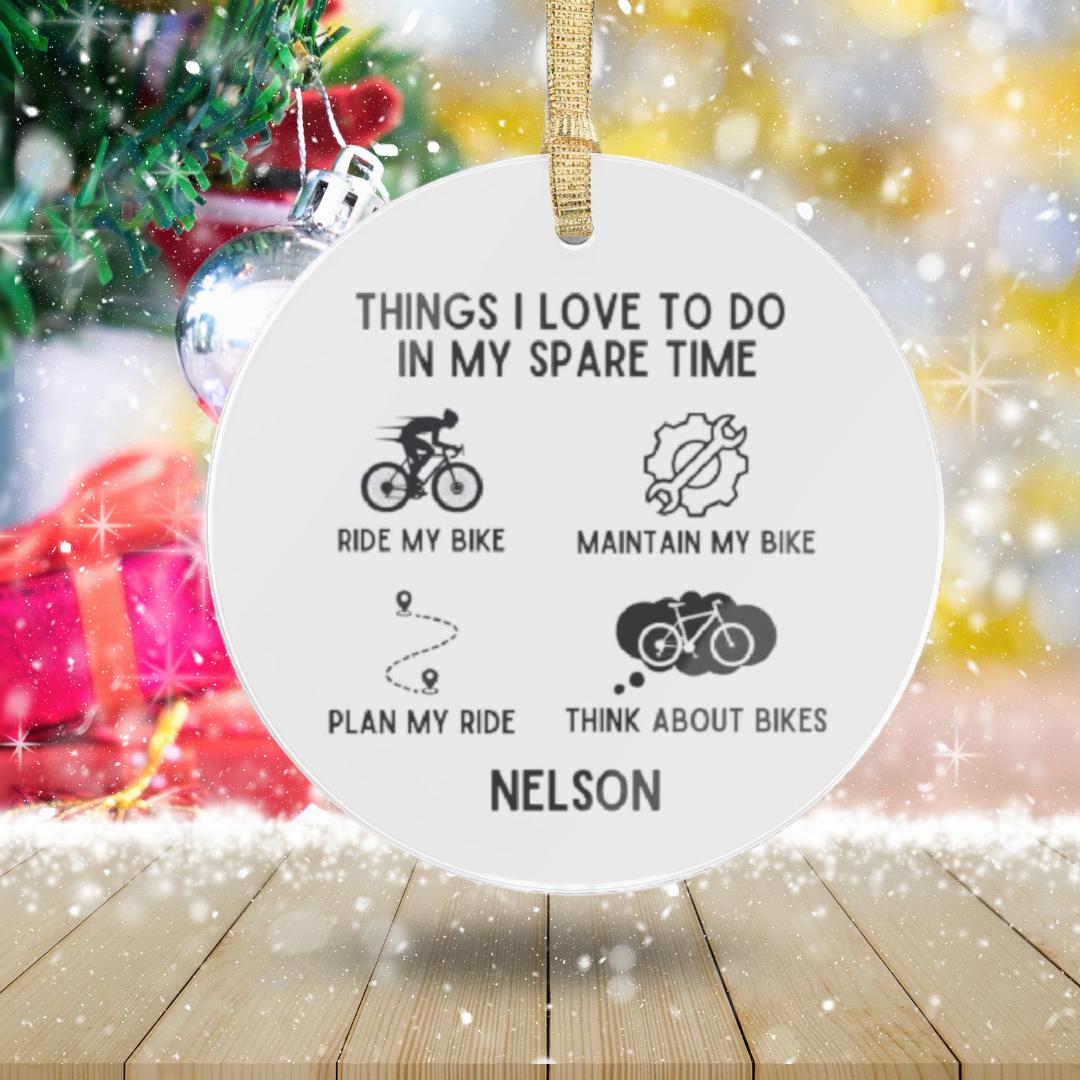 A transparent acrylic ornament, titled "Personalized Cyclist Ornament," humorously lists favorite cycling activities: riding, maintaining, planning rides, and thinking about bikes. The festive design includes a Christmas tree backdrop and can be customized with names like "Nelson," making it an ideal gift for bike enthusiasts.