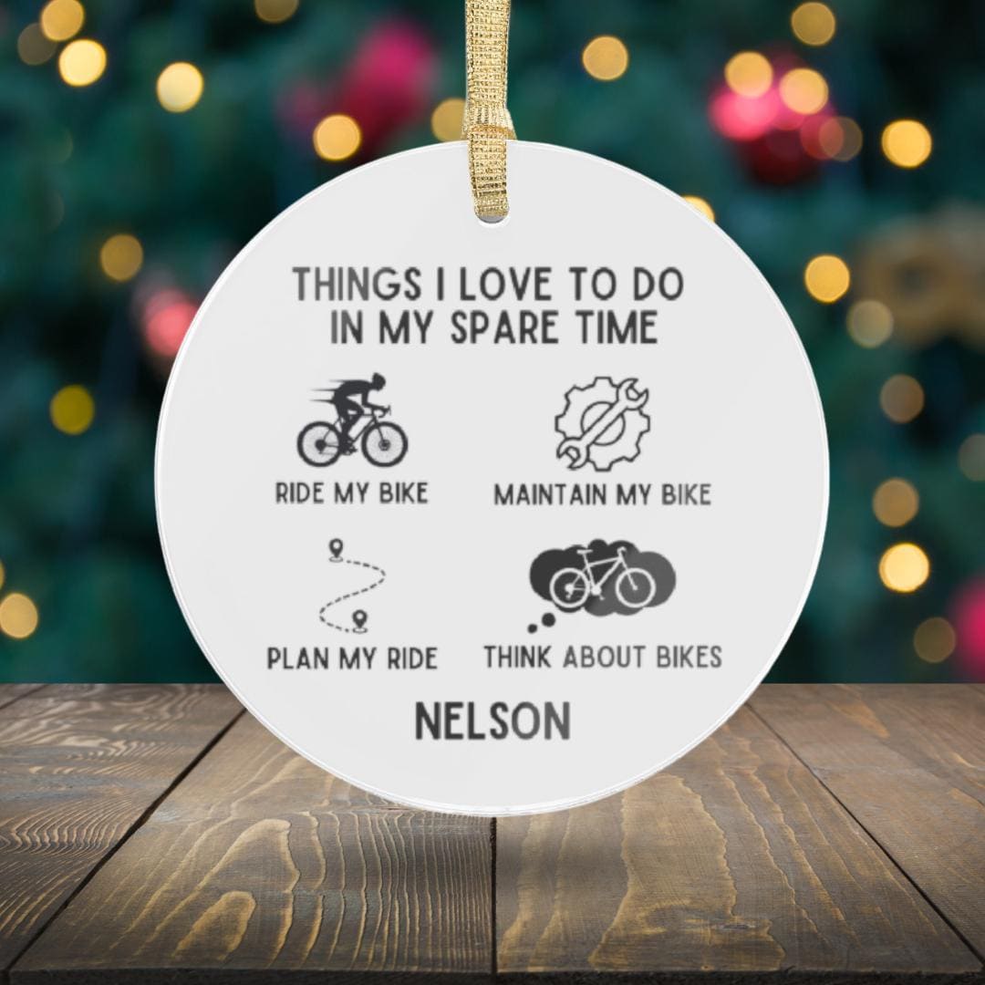 Transparent acrylic ornament with the text: "Things I love to do in my spare time: ride my bike, maintain my bike, plan my ride, think about bikes." This Personalized Cyclist Ornament makes an ideal gift for bike enthusiasts and cycling lovers, featuring a backdrop softly blurred by holiday lights.