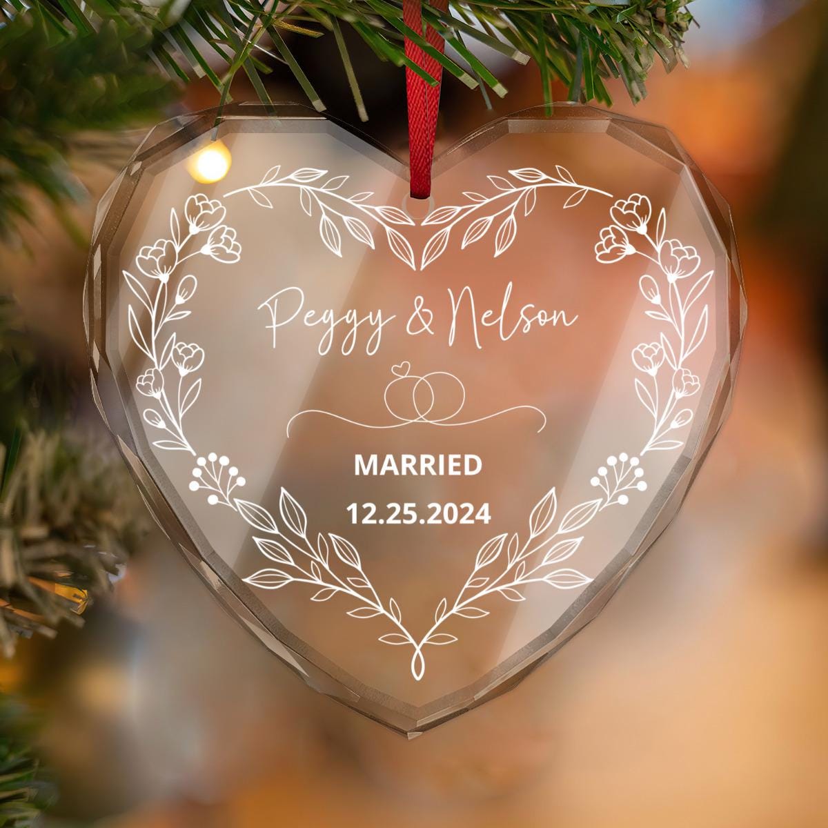 The heart-shaped crystal glass ornament features a floral design with "Peggy & Nelson," "Married," and date inscribed, making it a perfect keepsake gift for couples, elegantly hanging on a Christmas tree.