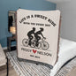 The Personalized Life Is A Sweet Ride Cycling Couple Heirloom Woven Blanket is an ideal gift for cycling couples, depicting love with two cyclists. It reads, "Life is a sweet ride with you every day," and can be personalized with names and a date like "Peggy ♥ Nelson Est. 2014.