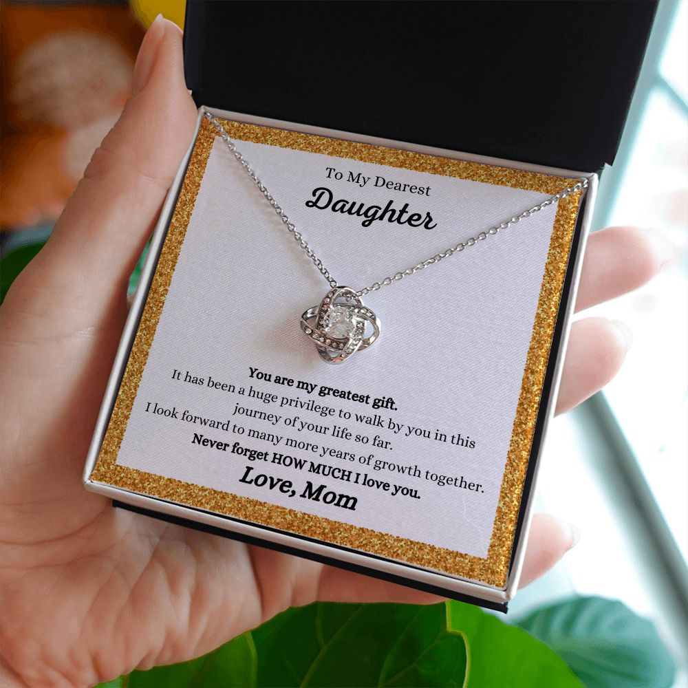 A woman holding a You Are My Greatest Gift Love Knot Necklace - Gift for Daughter from Mom from the ShineOn Fulfillment brand.