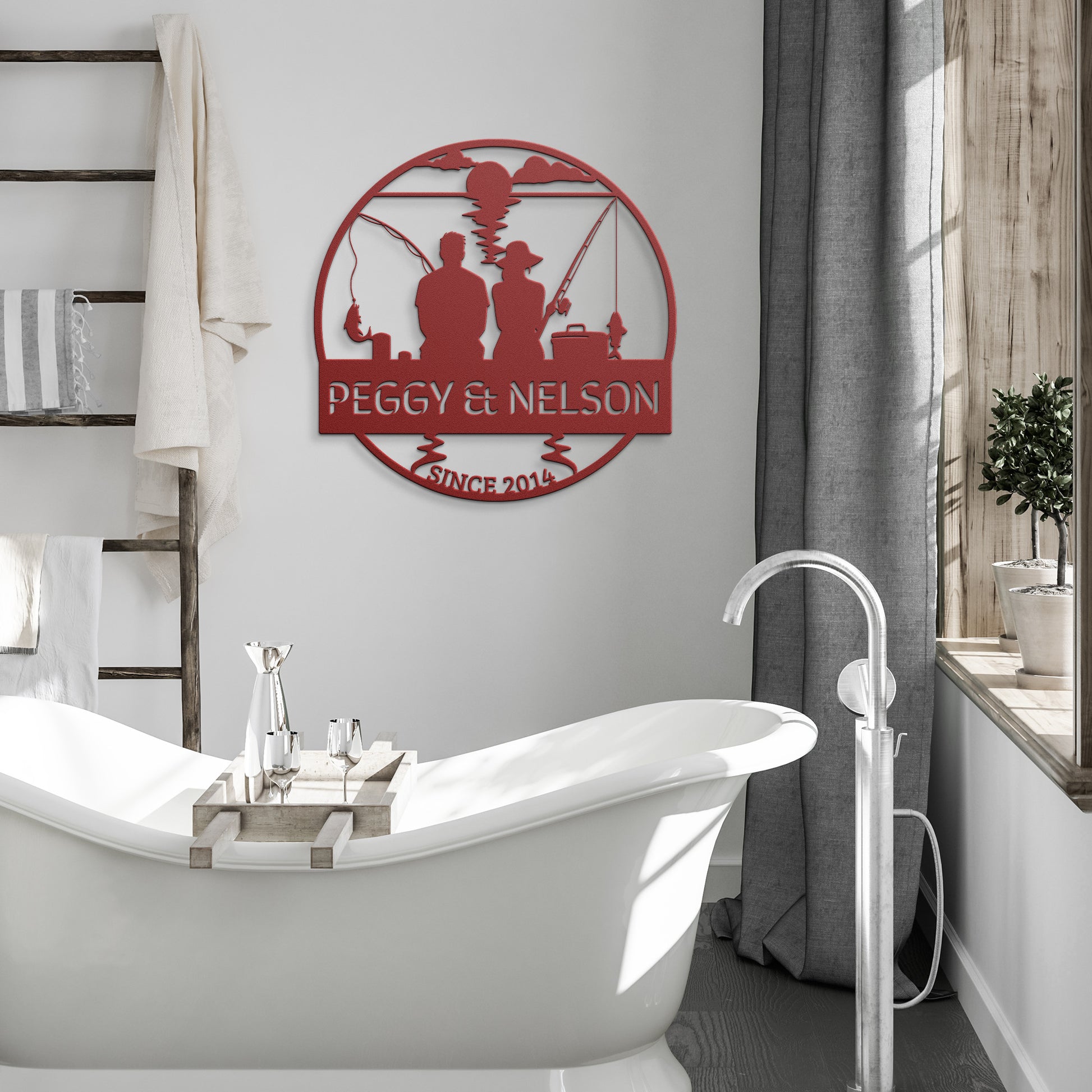 The Couple Fishing Together Metal Wall Art made from 18-gauge steel featuring the text "Peggy & Nelson Since 2015" is elegantly displayed above a freestanding bathtub in a modern, neutral-toned bathroom. The decor is complemented by a towel ladder and bathed in natural light streaming through a nearby window.
