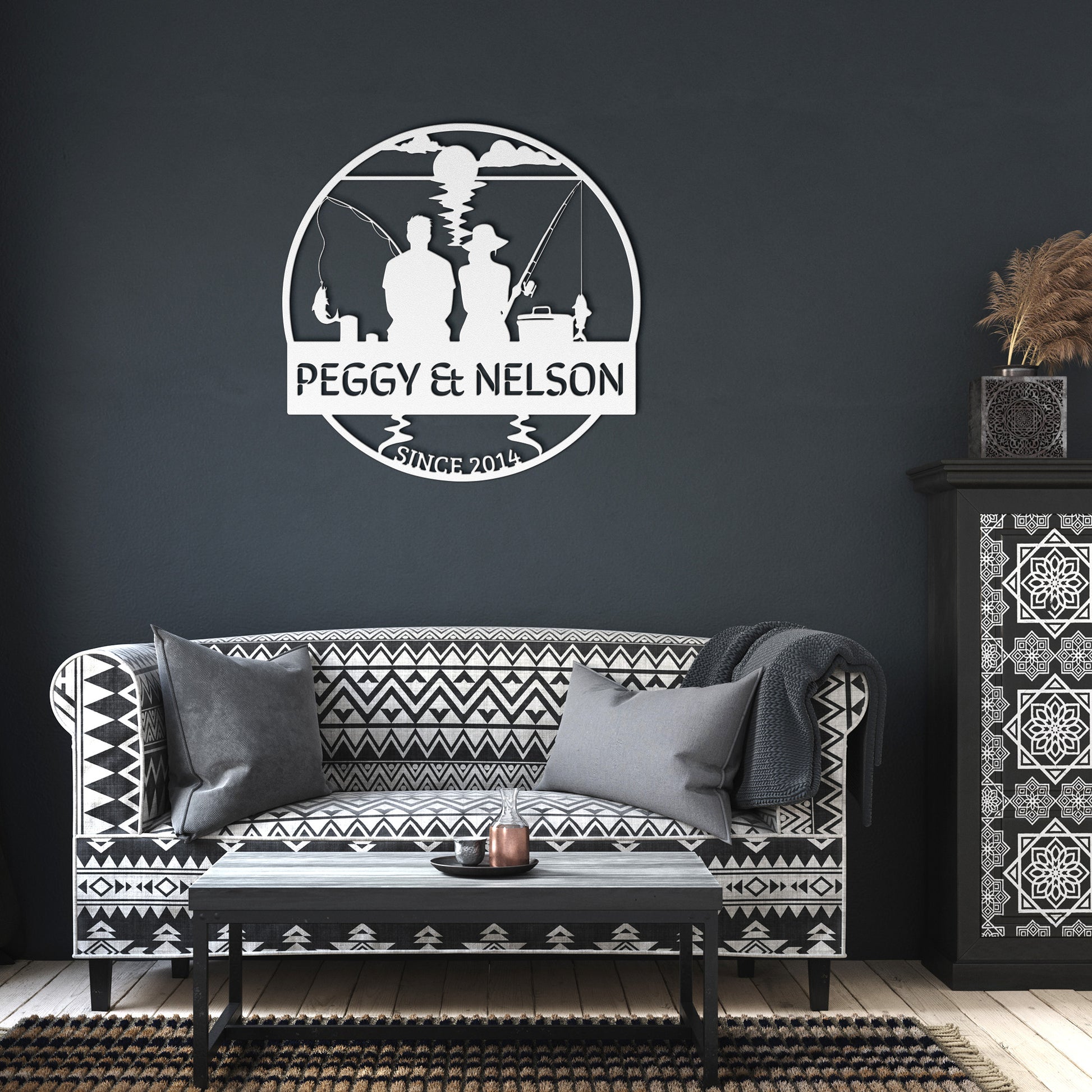 A living room with a black and white patterned couch, a decorative cabinet, and custom "Couple Fishing Together Metal Wall Art" made from 18 gauge steel reading "Peggy & Nelson, Since 2014" showcases stunning home decor.