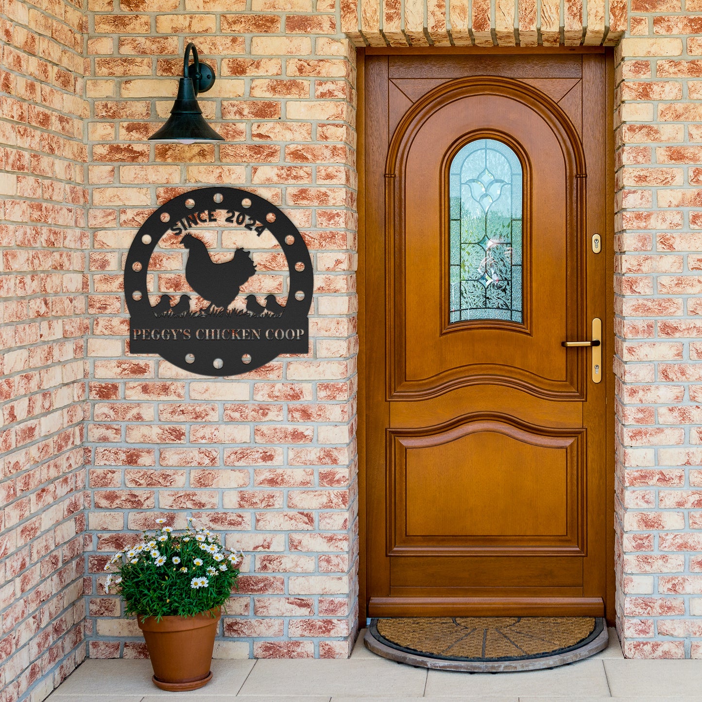 A wooden door with a stained glass window is set in a brick wall. A stylish "Custom Chicken Coop Metal Sign" crafted from 18 gauge steel reads, "Peggy's Chicken Coop Since 2022." To enhance the charm of this home decor, a potted plant with white flowers is placed nearby.