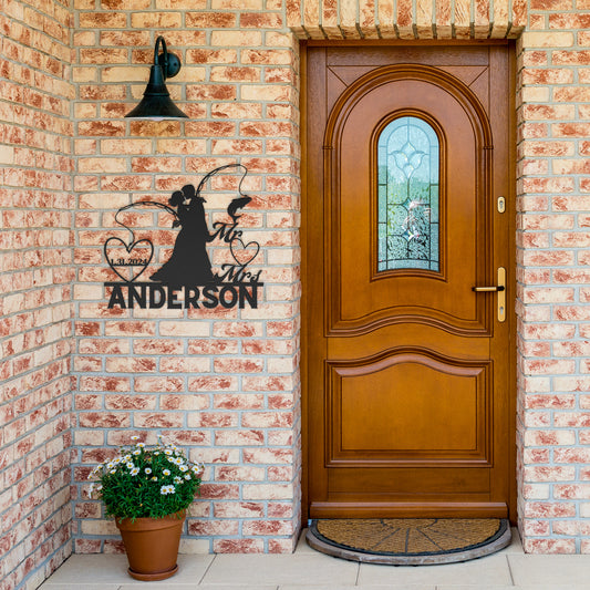 A wooden front door with stained glass and a Custom Fishing Couple Metal Wall Art reading "the anderson" next to a wall-mounted bell on a brick wall.