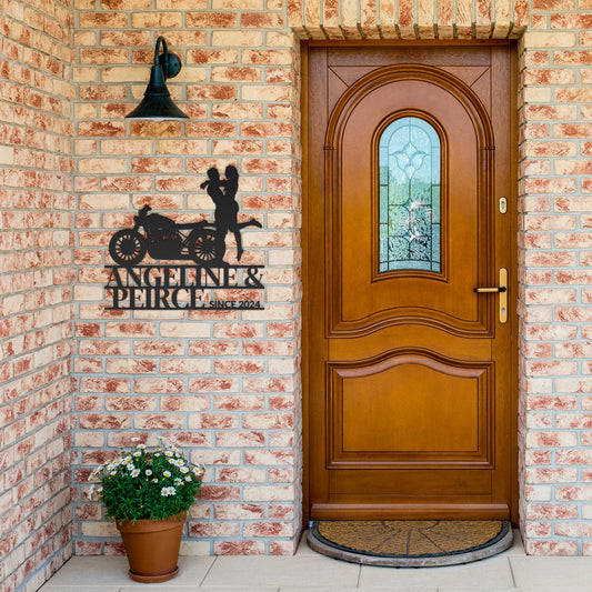 A wooden front door with stained glass, flanked by brick walls, featuring a Custom Motorcycle Couple Metallic Wall Art and a hanging bell.