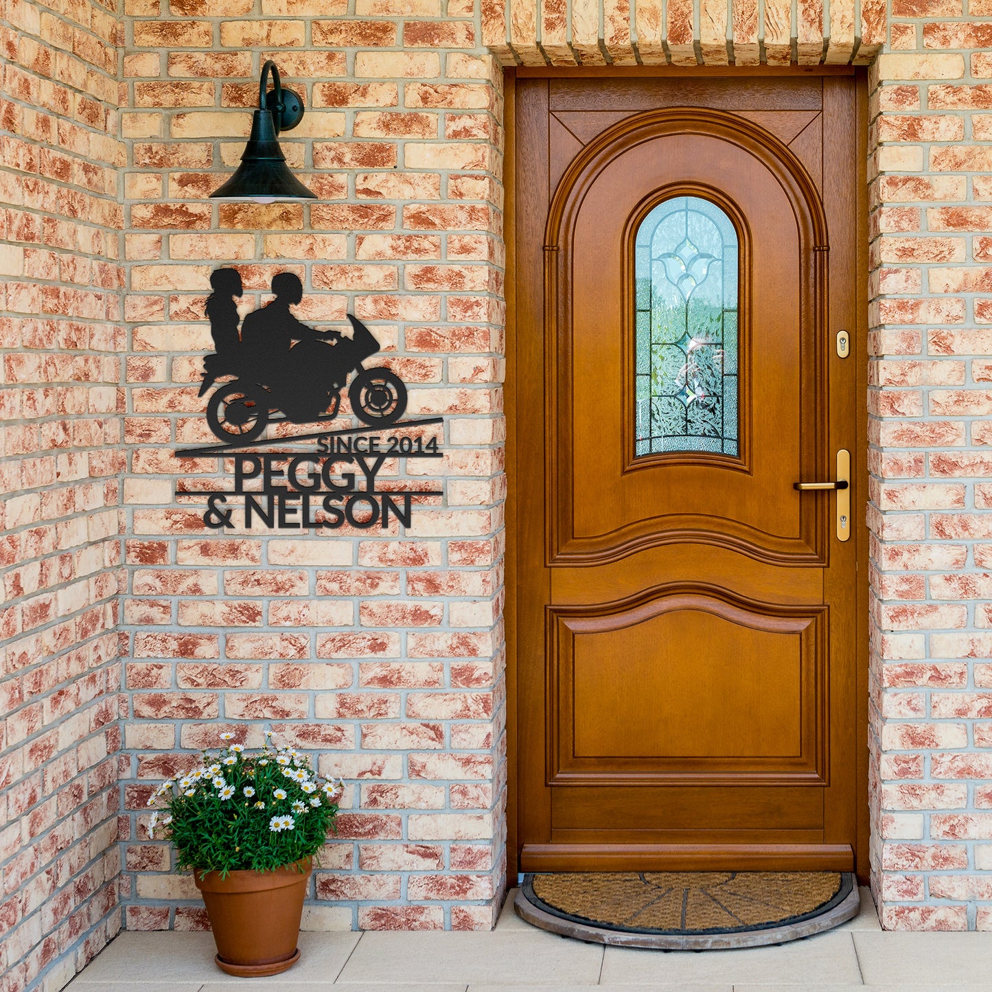 A wooden front door with a stained glass window, set in a brick wall. Next to the door, a Custom Motorcycle Couple Metallic Wall Art featuring a motorcycle, with the names "Peg".