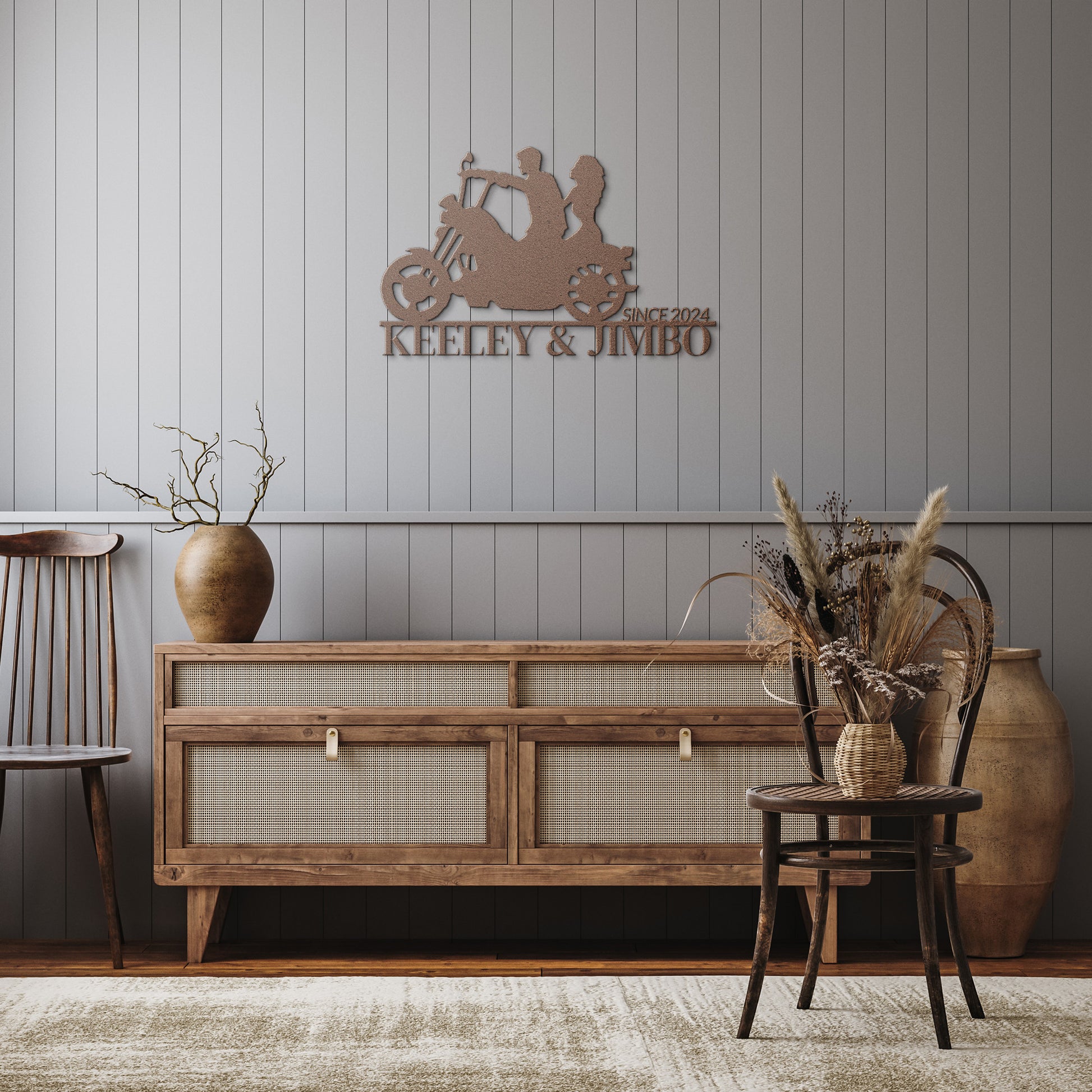 The "Custom Motorcycle Couple Metallic Wall Art" features a detailed motorcycle design and the text "Keeley & Jimbo, since 2024," elegantly displayed on a gray paneled wall above a wooden console adorned with various home decor items.
