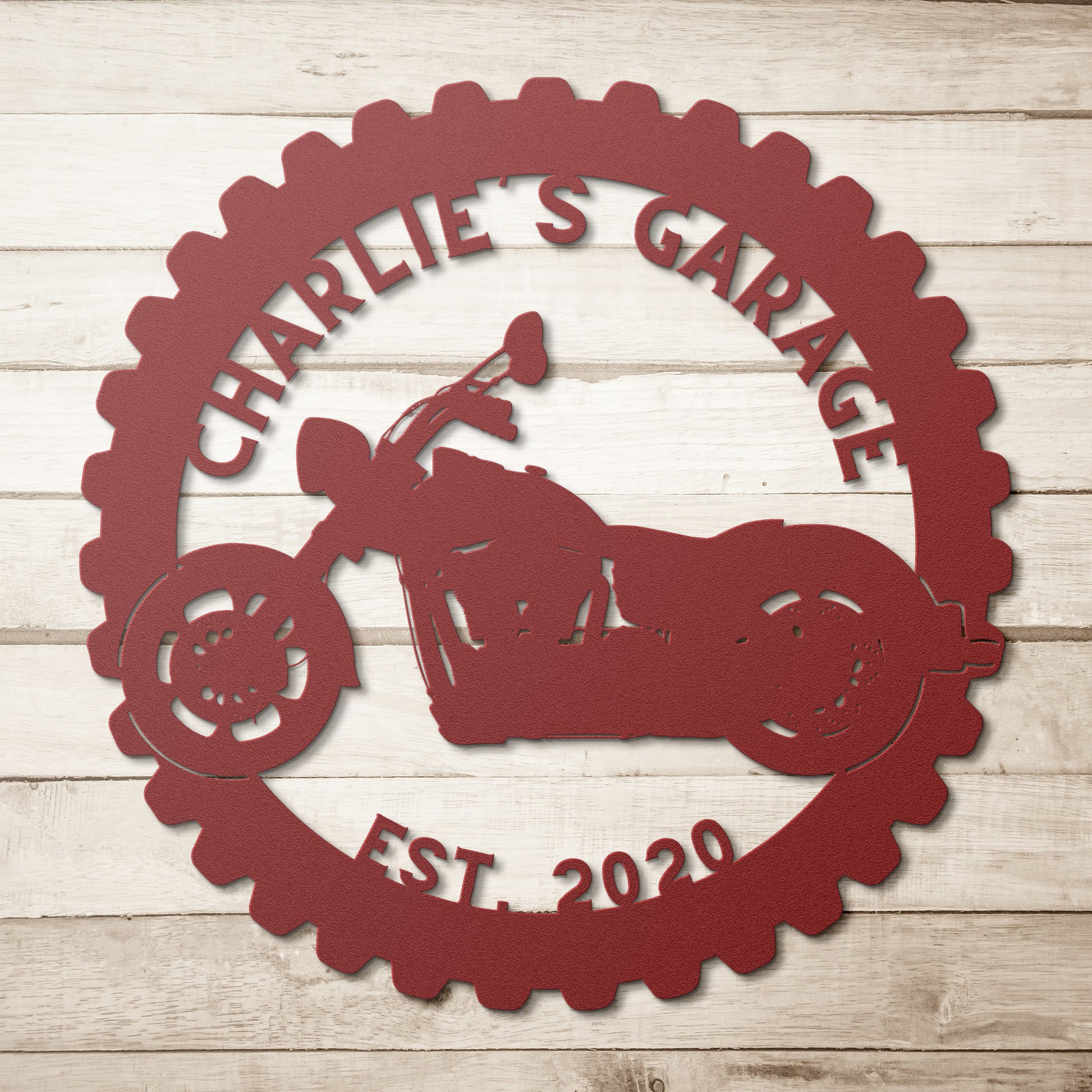 A wooden front door set in a brick wall with a stained glass window. A Custom Motorcycle Garage Sign reading "Charlie's Garage Est. 2021" and a black light are mounted to the wall, enhancing the home decor. A potted plant sits beside the door.