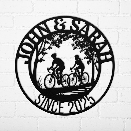 The Personalized Cyclist Couple Metal Wall Art showcases two people riding bicycles under trees, customized with names like “John & Sarah” and “Since 2025,” making it striking personalized decor for your white brick wall.