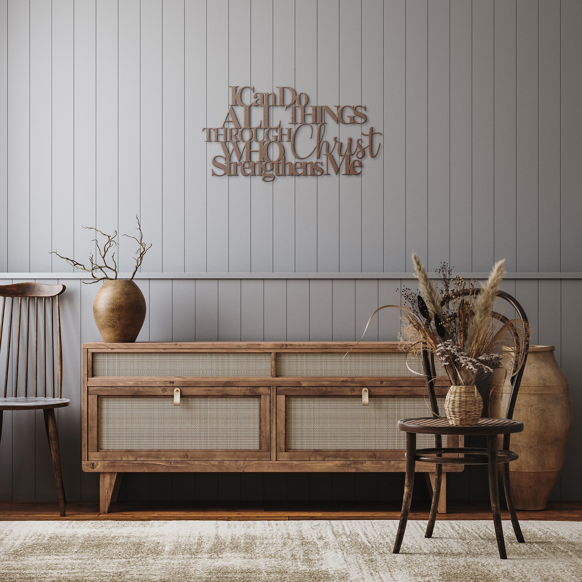 A wooden sideboard with decorative vases and dried plants is placed against a paneled wall, featuring the "I Can Do All Things Through Christ Who Strengthens Me Christian Metal Sign" crafted from 18 gauge steel with a religious quote displayed above it. Two chairs are positioned on either side of the sideboard, completing the home decor ensemble.