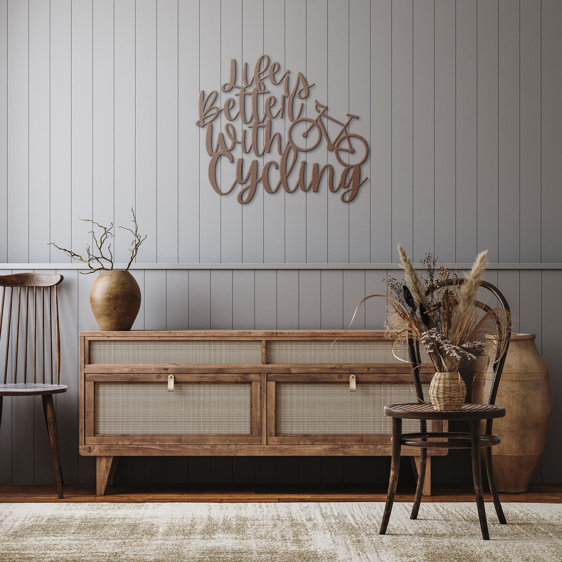 A brick wall with a wooden door, a potted plant, a black outdoor light, and the "Life is Better with Cycling Metal Sign - Road Bike Edition," reading "Life's Better with Cycling" alongside a bicycle graphic, perfect for stylish home decor.