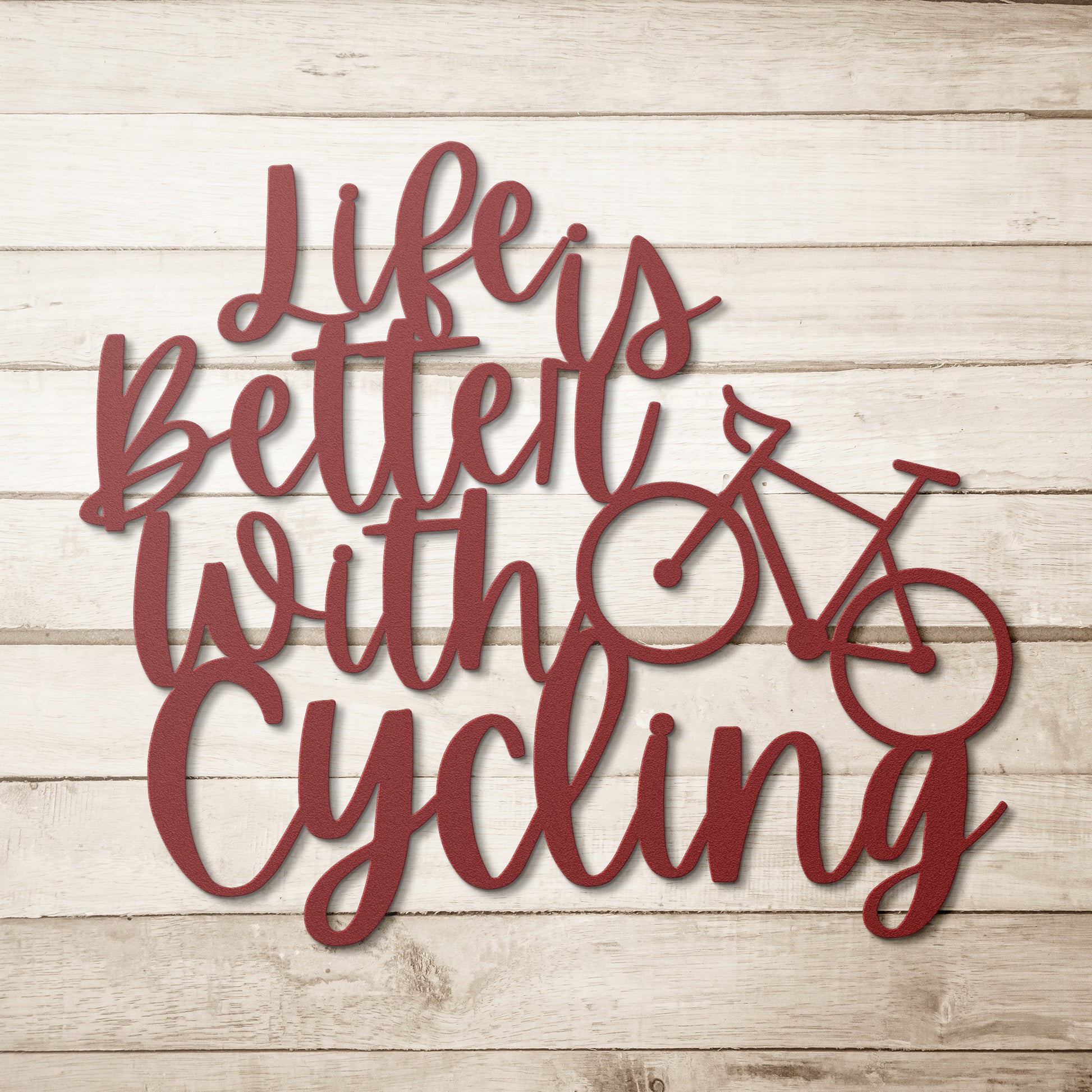A brick wall with a wooden door, a potted plant, a black outdoor light, and the "Life is Better with Cycling Metal Sign - Road Bike Edition," reading "Life's Better with Cycling" alongside a bicycle graphic, perfect for stylish home decor.