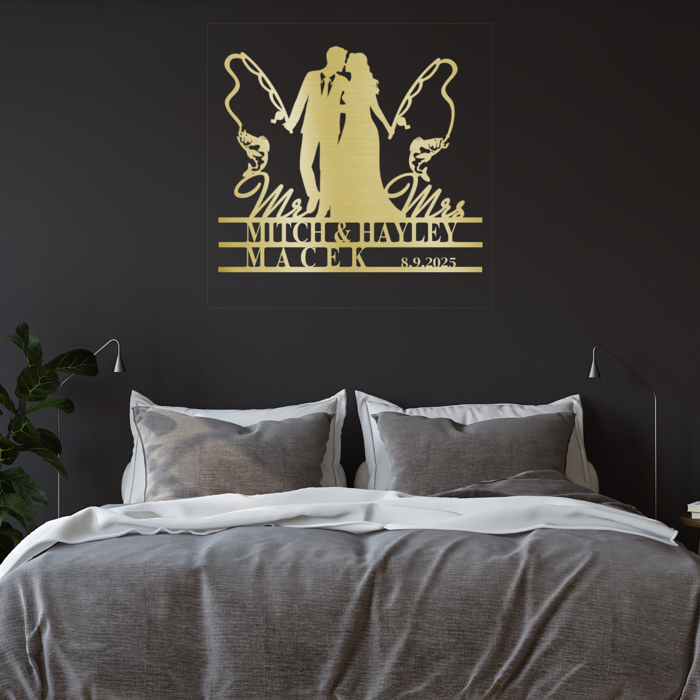 A modern bedroom includes a gray upholstered bed, white bedding, and, above the bed, a Personalized Fishing Couple Wedding Metal Sign with "Mr & Mrs Mitch & Hayley Macek 8.9.2025." A leafy plant decorates the left side.
