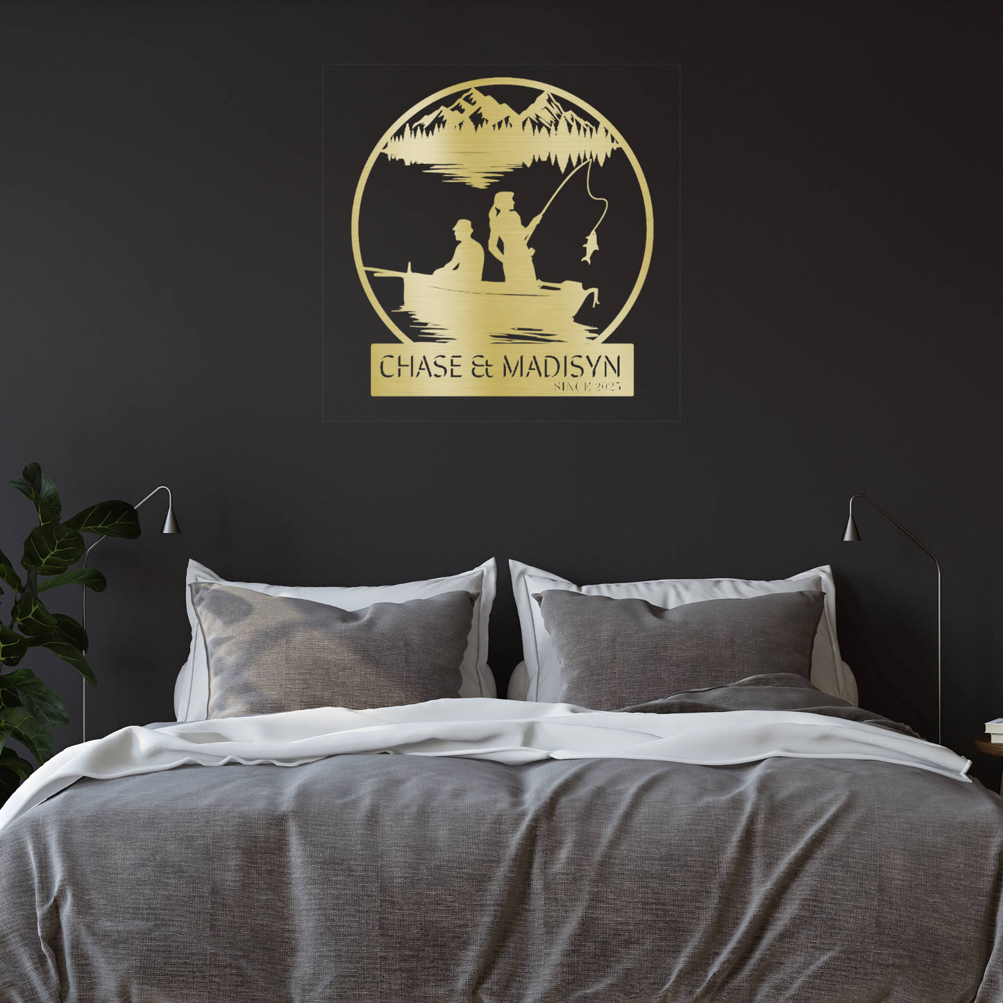 A cozy bedroom features a gray bed with white bedding. Above the bed hangs the Custom Fishing Couple Metal Sign, personalized with two people fishing in a boat, mountains, "Chase & Madisyn," and "Since 2023.